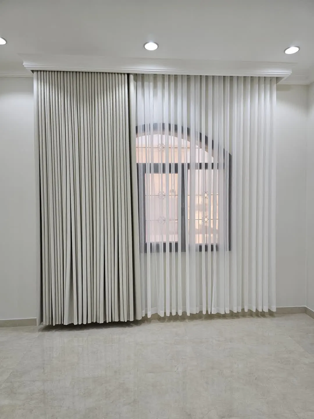 Floor-to-ceiling curtains on a ceiling track with white sheer layer beside an arched window
