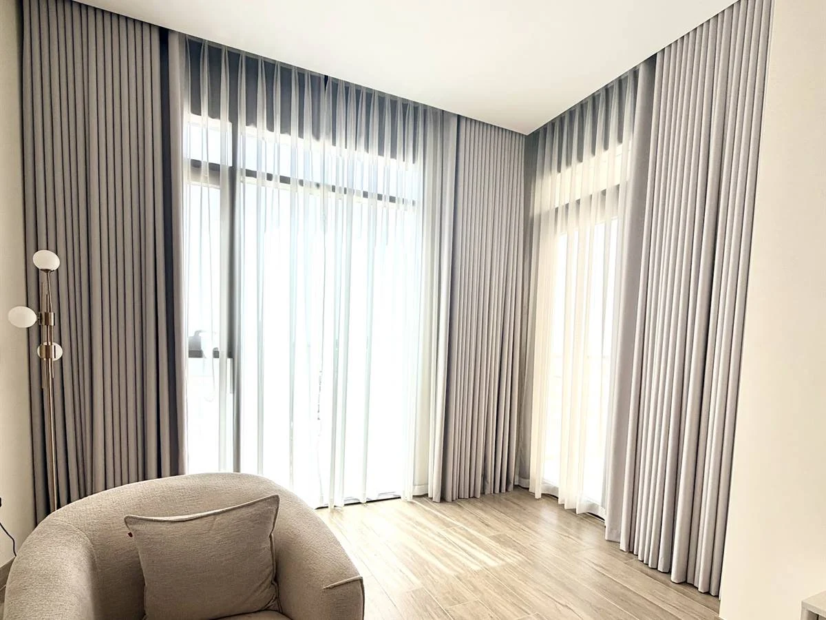 Grey made-to-measure curtains with white sheers across tall corner windows in Lara's Doha apartment